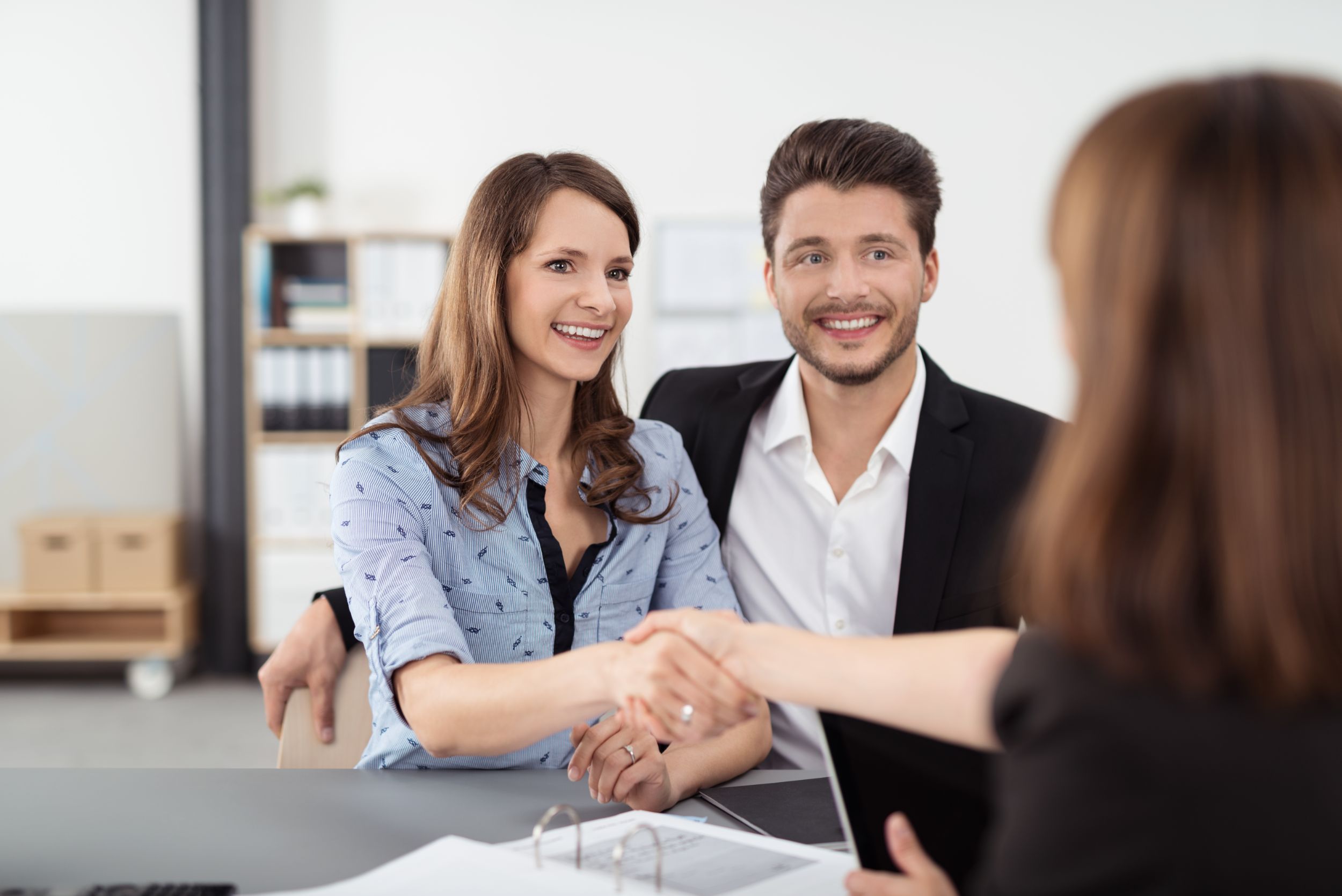 Happy Young Professional Couple Shaking Hands with a Real Estate Agent After Some Business Discussions Inside the Office